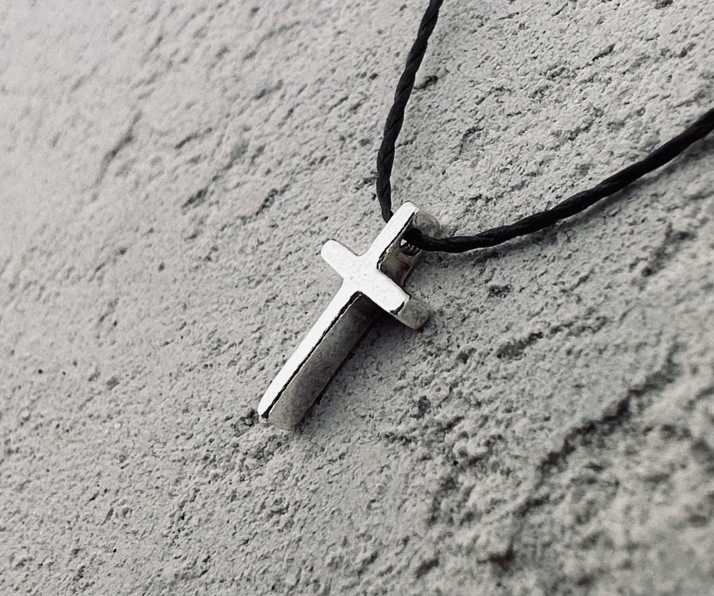 Sterling silver tiny cross charm on the concret wall.