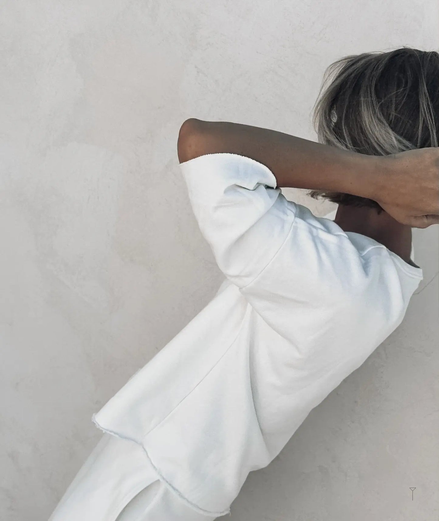 A woman leaning against a wall wearing white tulua top.