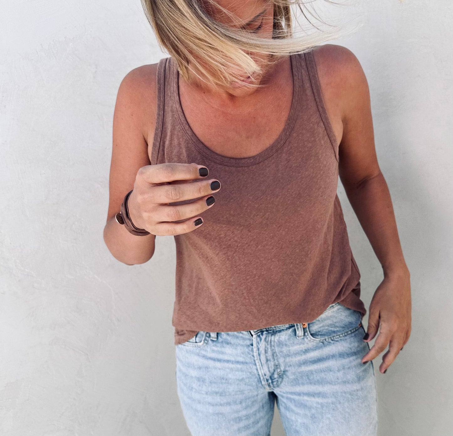 A woman with a windy hair wearing a brown tank top and jeans.