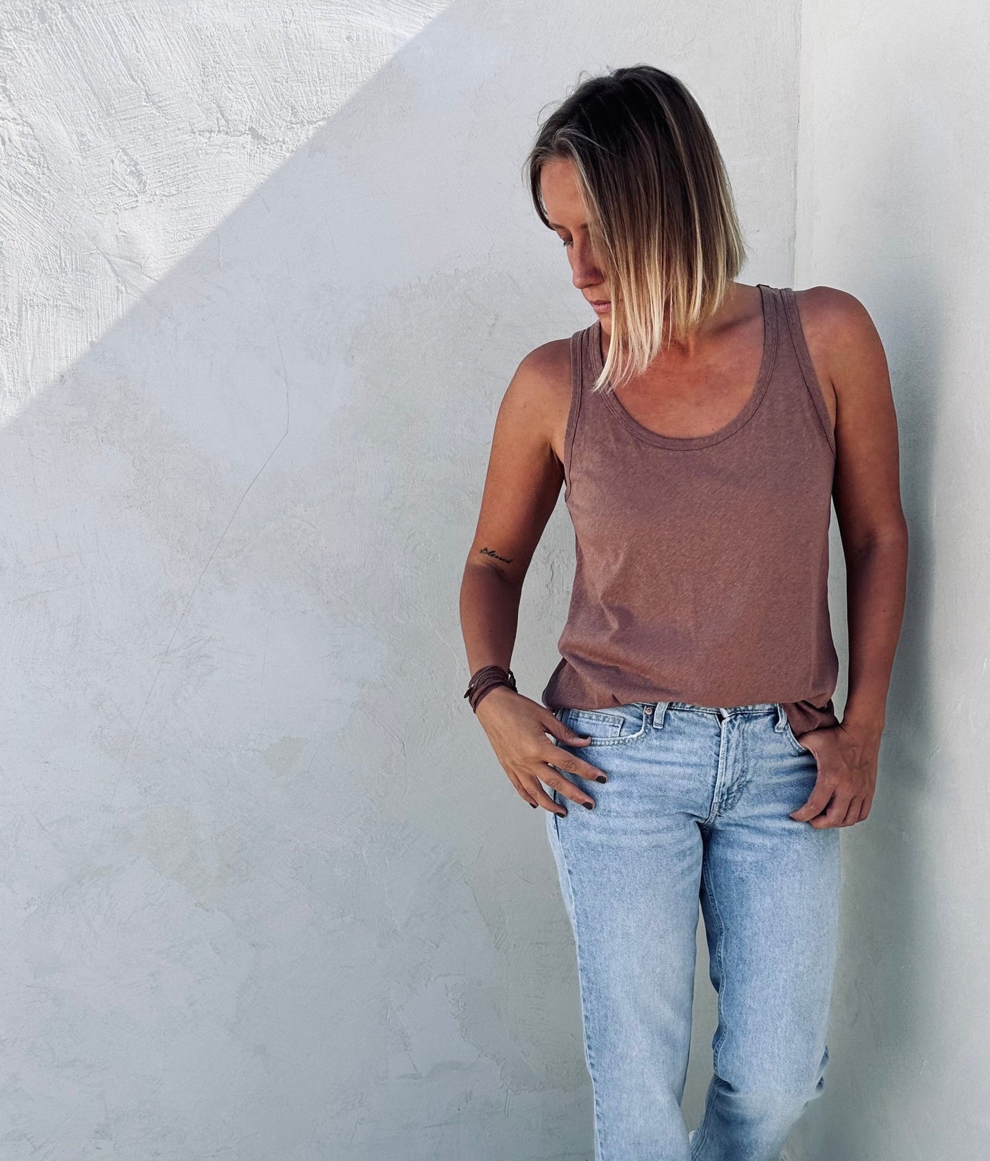 A woman near the wall posing with a brown tank top.