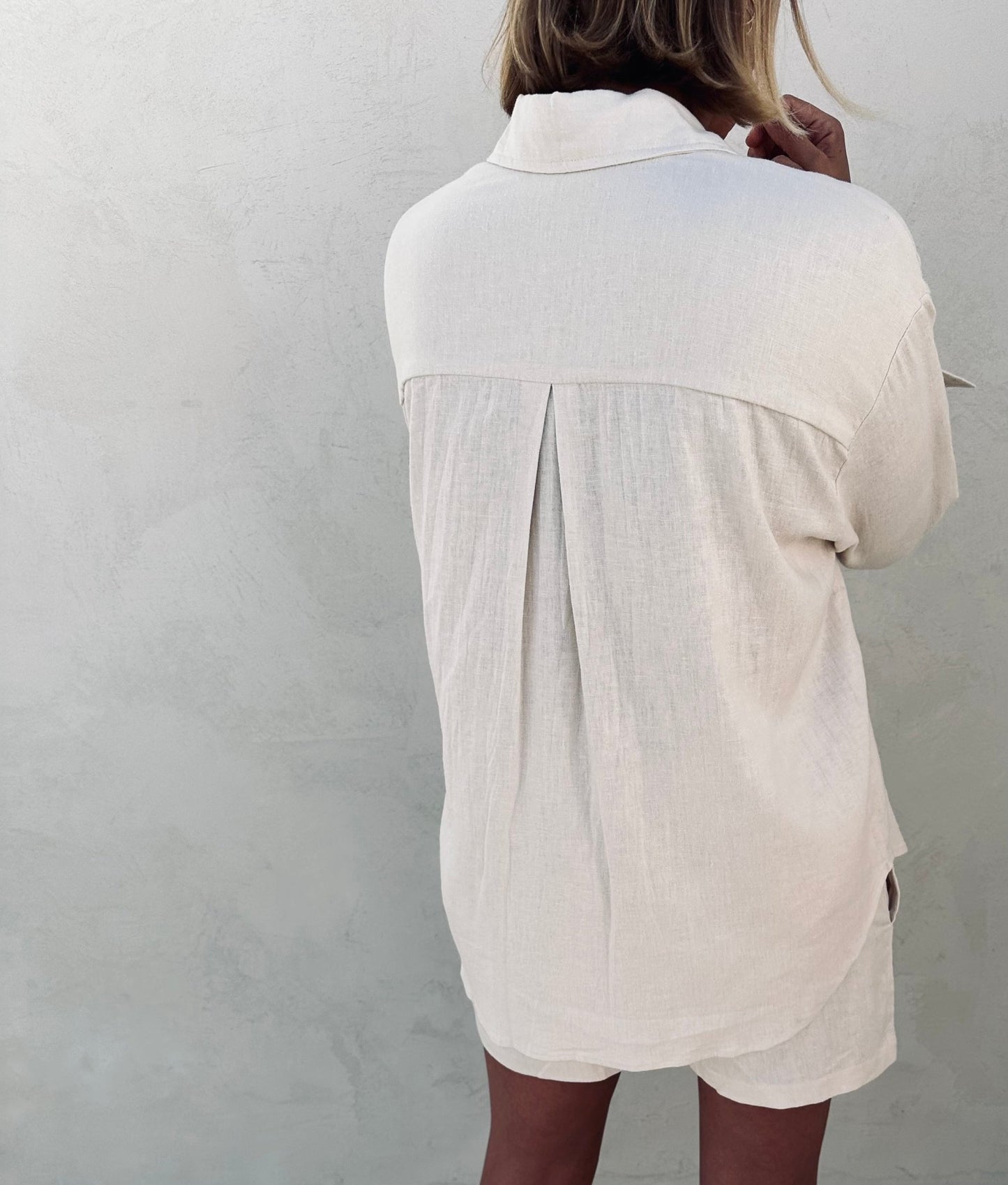 A back of a woman wearing ivory linen shirt and shorts.
