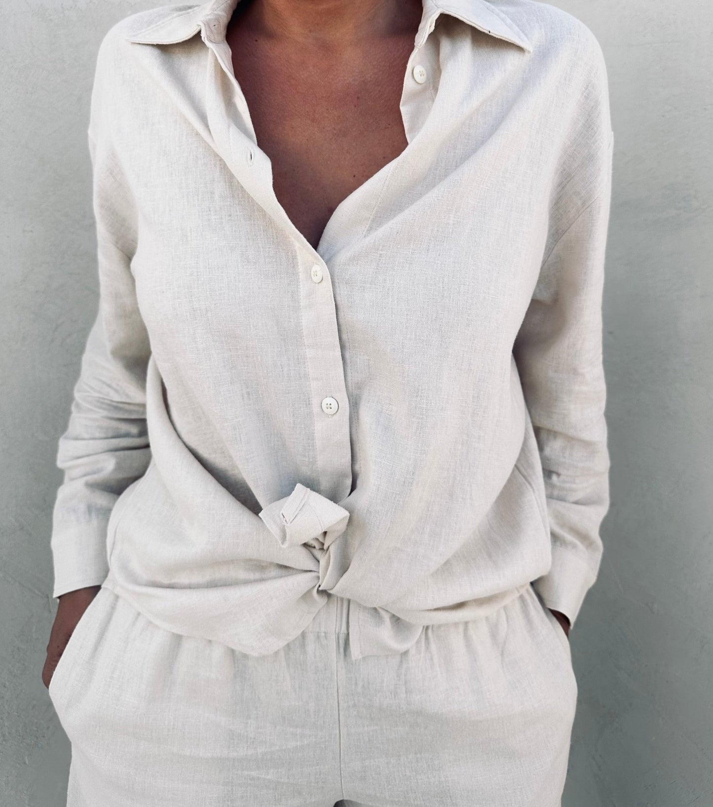 A woman wearing ivory linen shirt and shorts knotted in front.