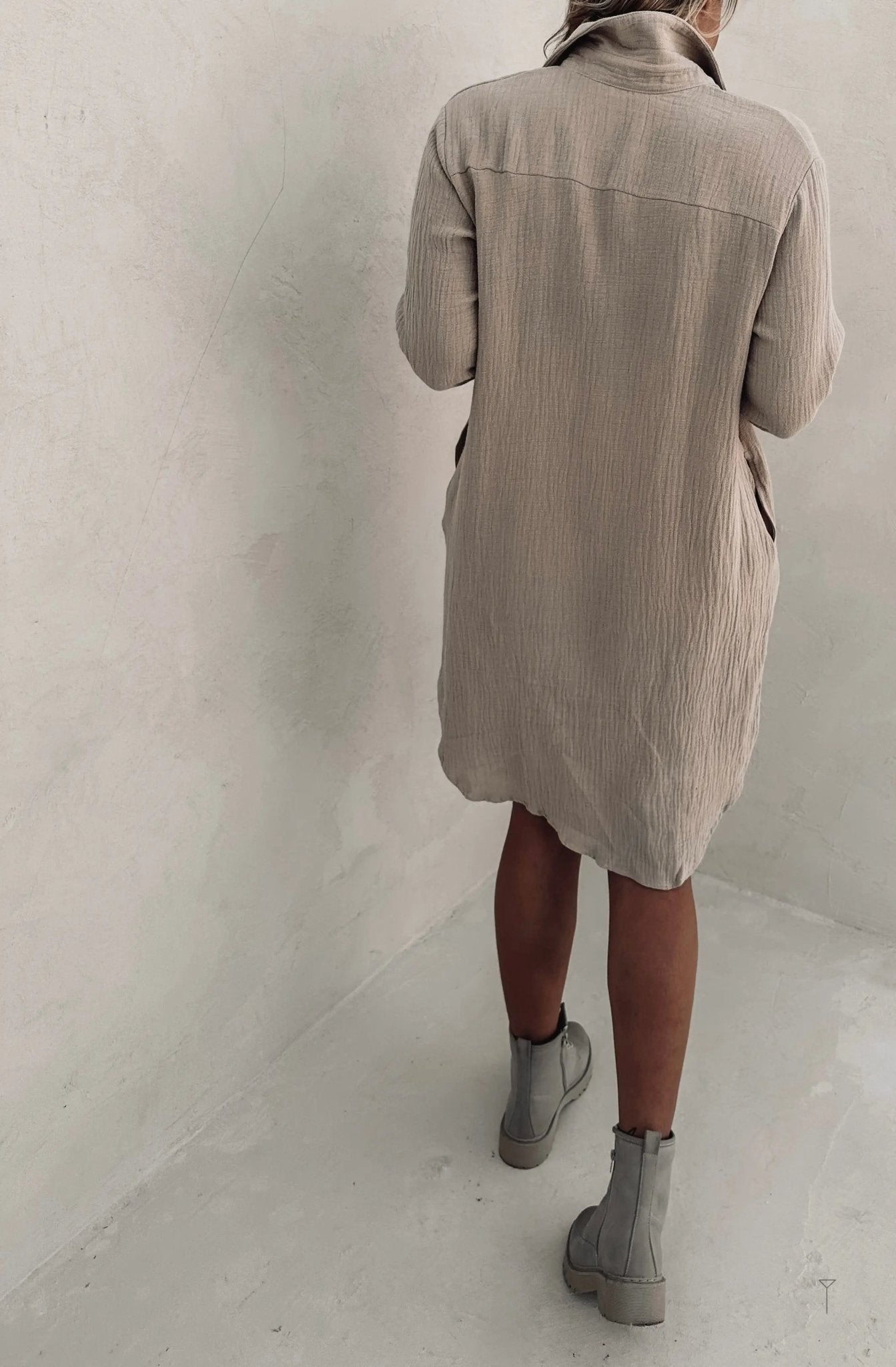 AThe back view of a woman wearing a beige shirt dress.