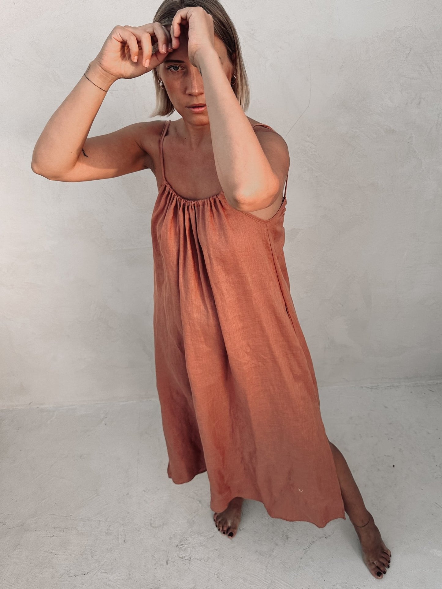 A woman is posing in a long rust color linen dress.
