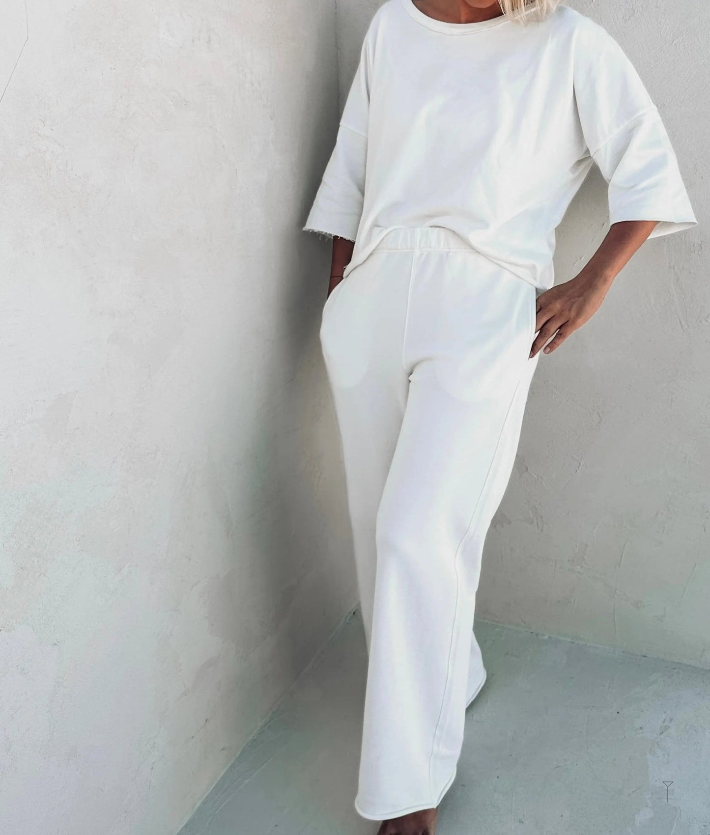 A woman wearing off white pants and a white top