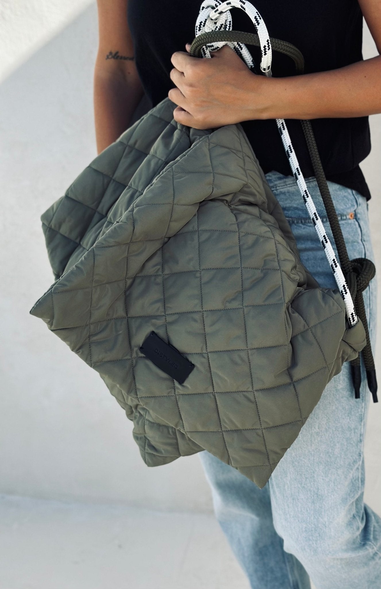 A woman holding a big quilted tote bag in olive green.