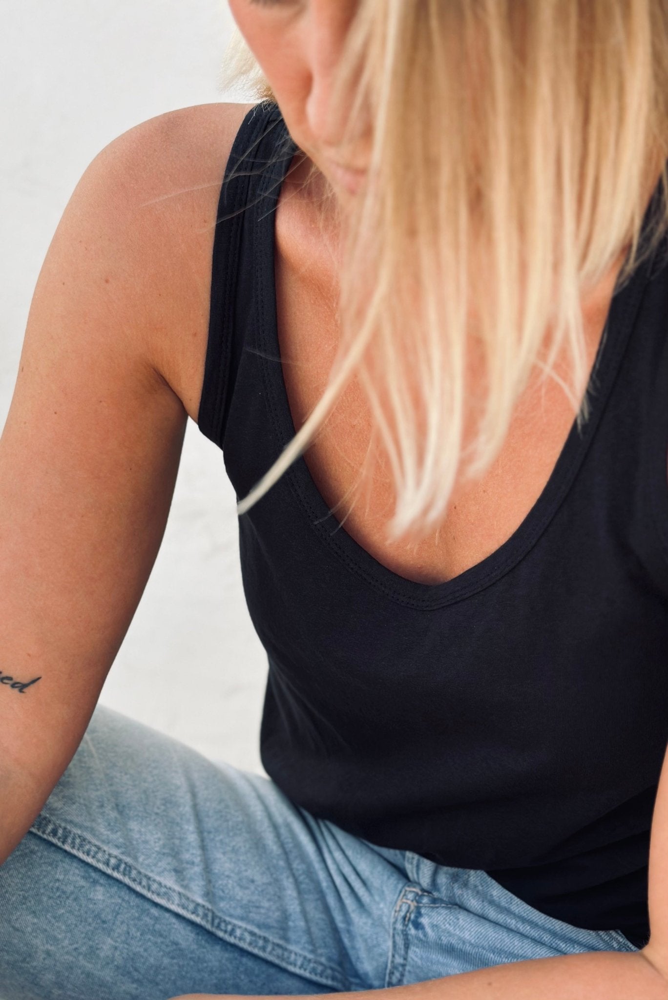 A woman with a black tank top and tatoo on her arm.