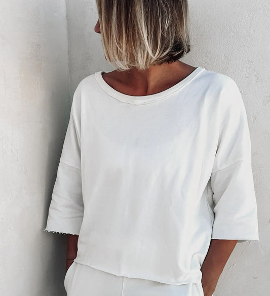 A woman leaning against a wall wearing white clothing. 