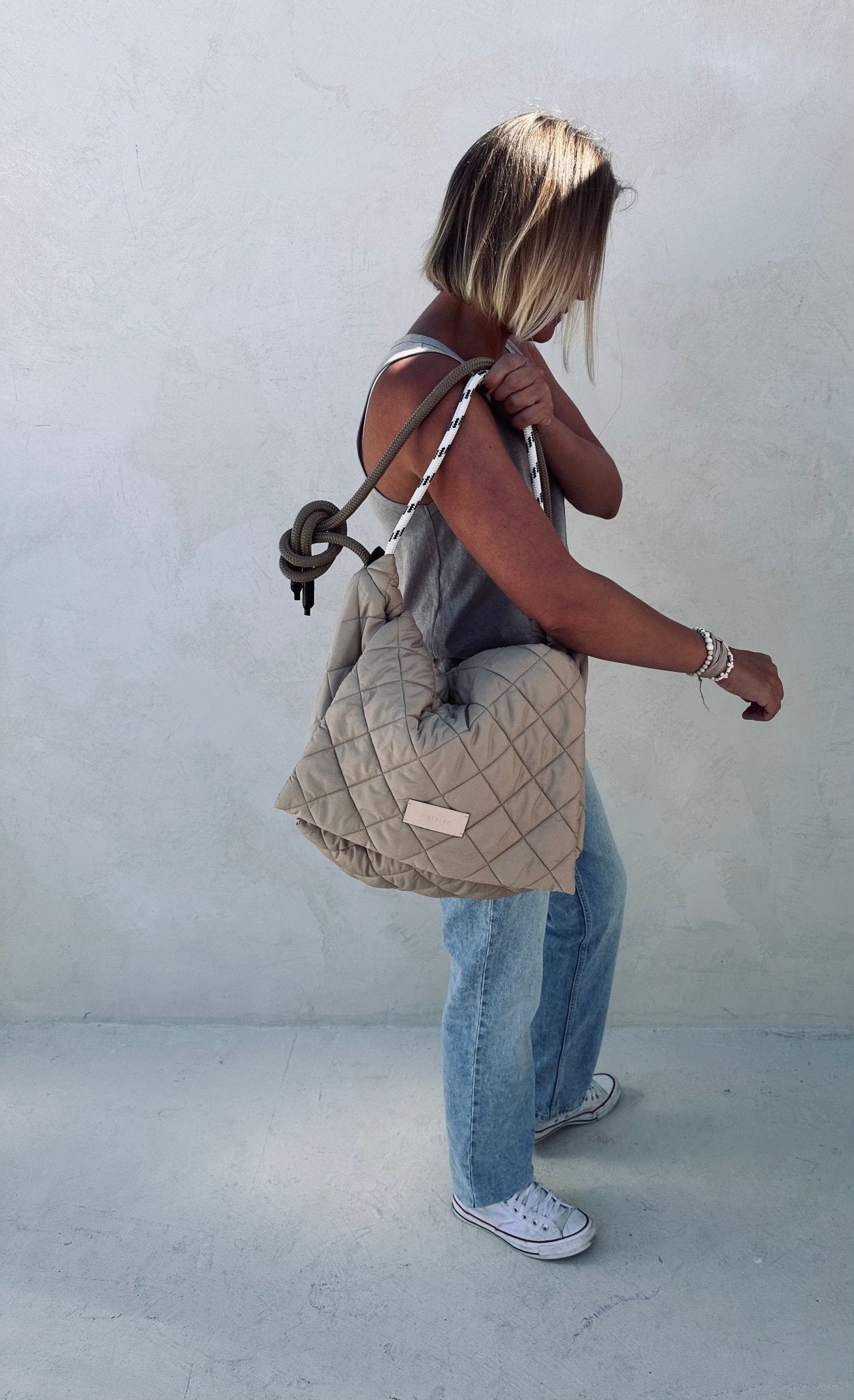 A woman holding a beige quilted tote bag.  
