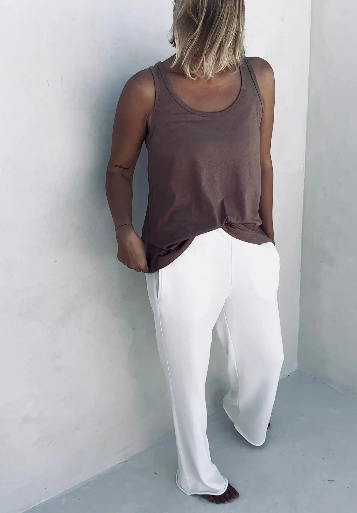 A woman in a front of the wall wearing white wide pants and a tank top