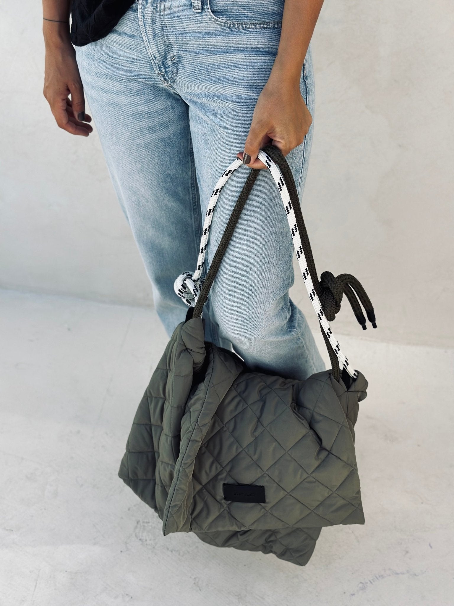 A woman holding a quilted tote bag in olive green. 