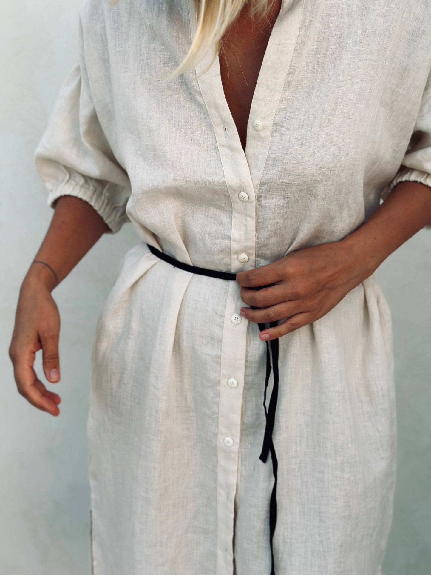 A woman in a white linen dress with a black tiny belt. 
