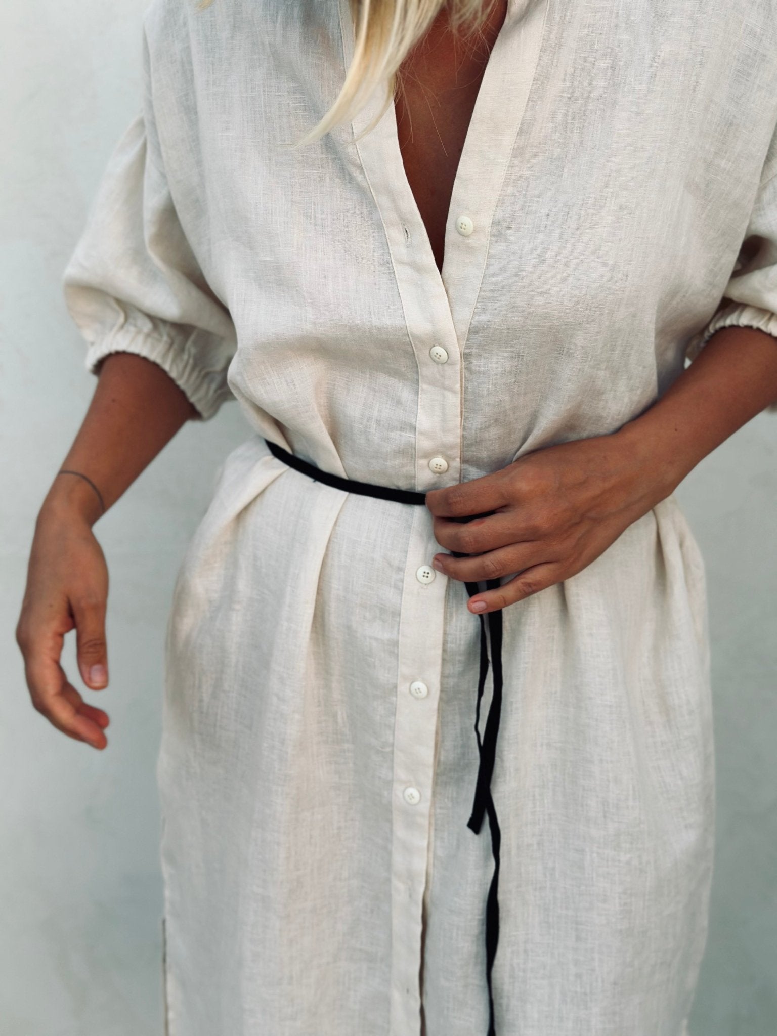 A woman in a white linen dress with a black tiny belt. 