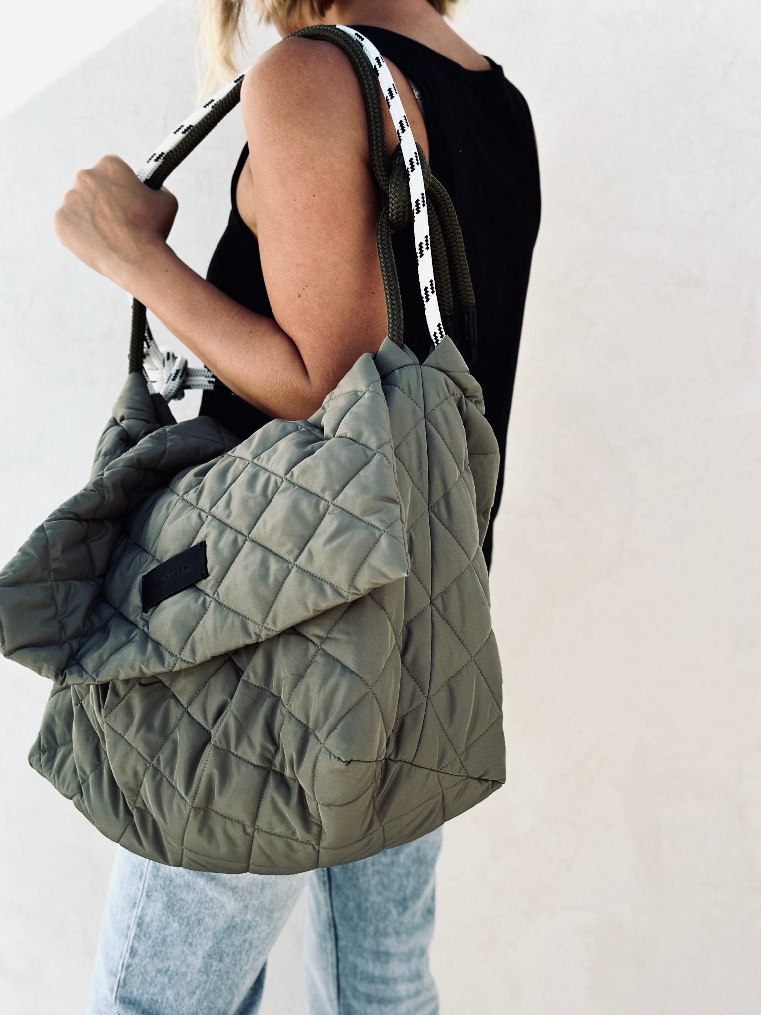 A woman holding a military green quilted bag.  