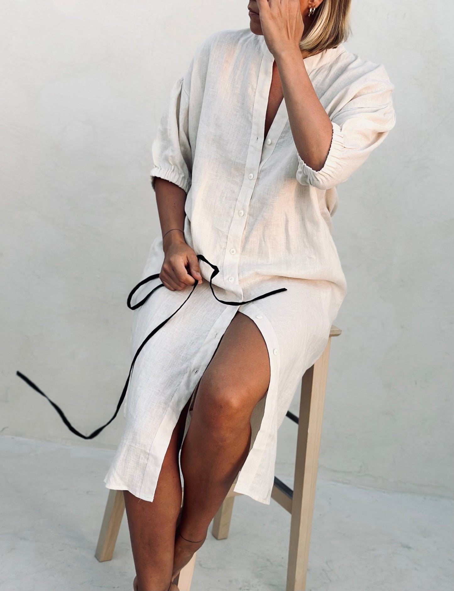 A woman in a white linen dress sitting on a high chair. 