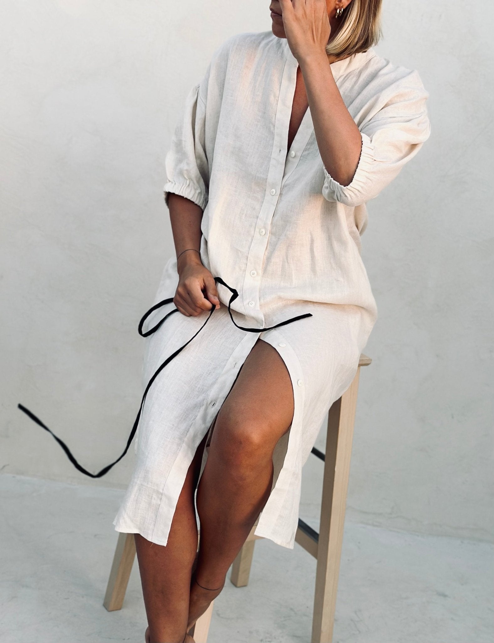 A woman in a white linen dress sitting on a high chair. 