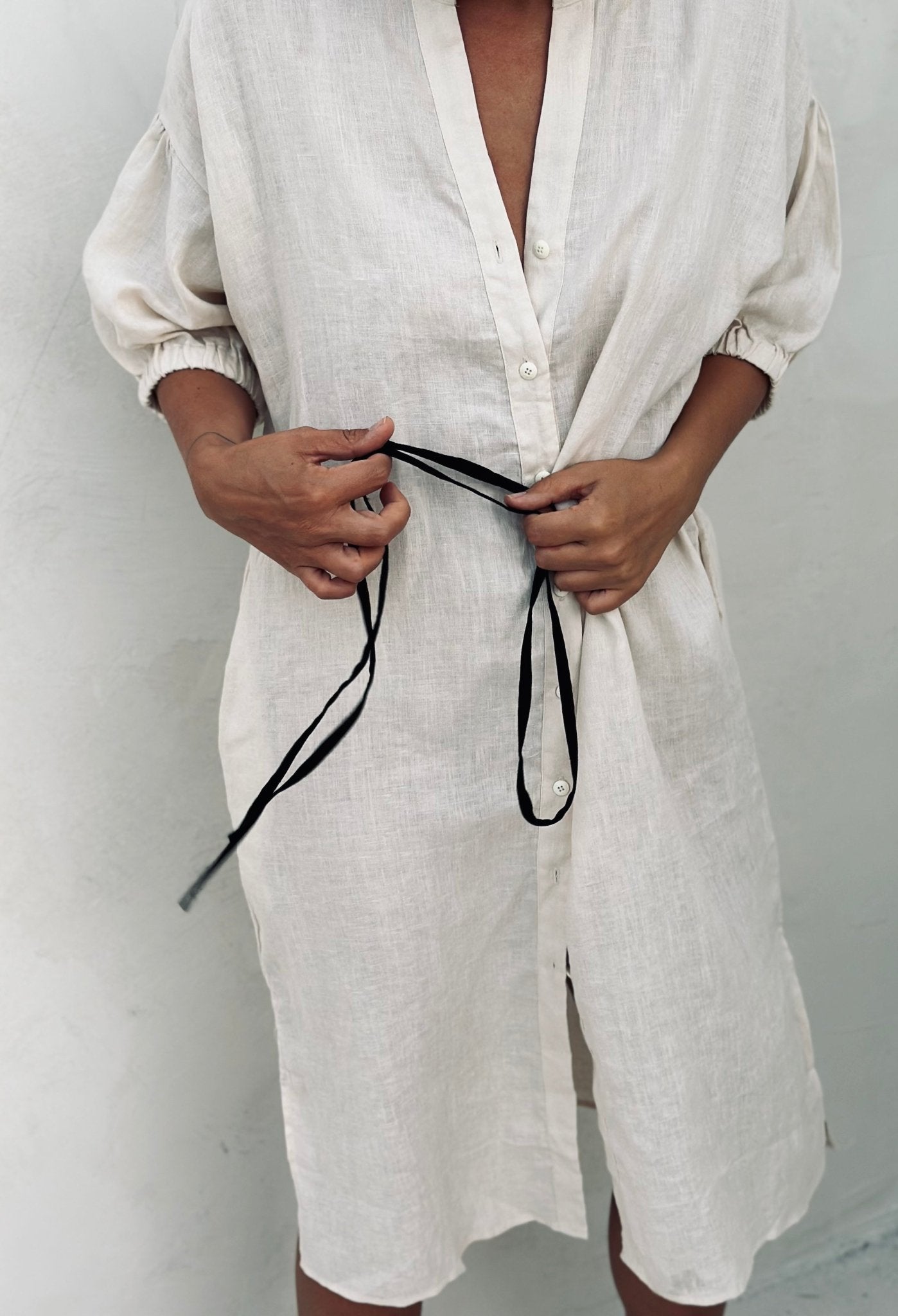 A woman in a white shirt dress holding a black tiny stripe. 